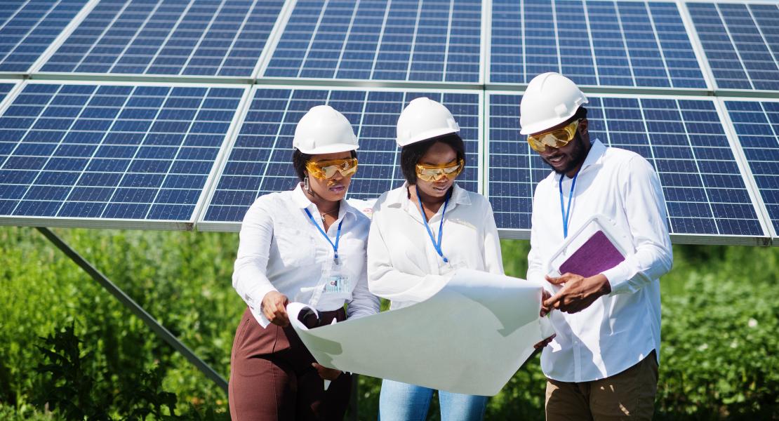 Three people wearing hard hats reviewing document in front of solar farm